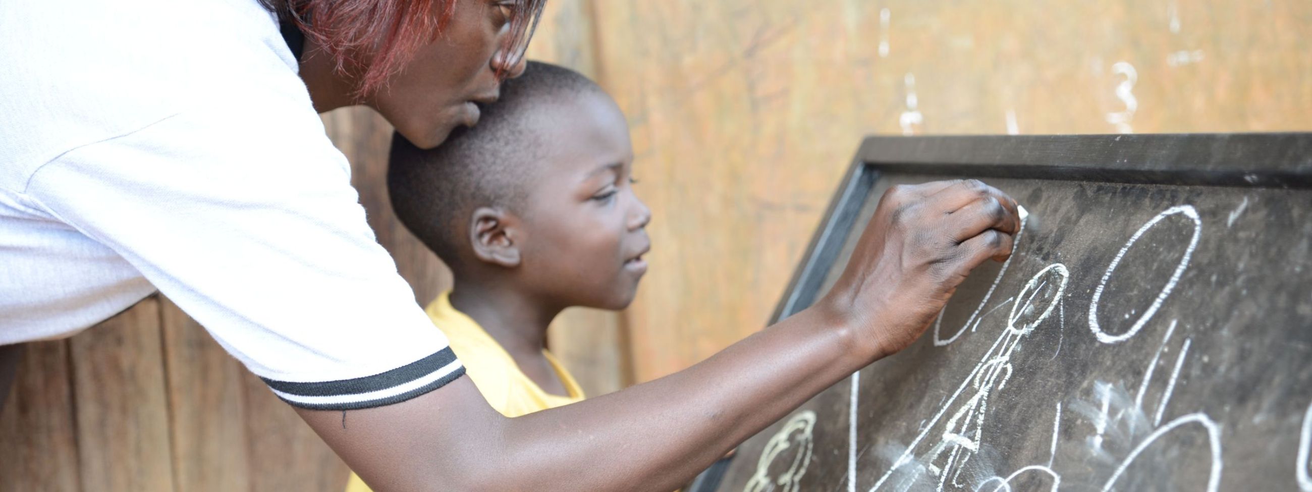 A woman and a child write on a blackboard with chalk