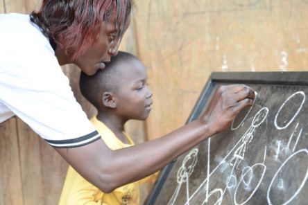 A woman and a child write on a blackboard with chalk