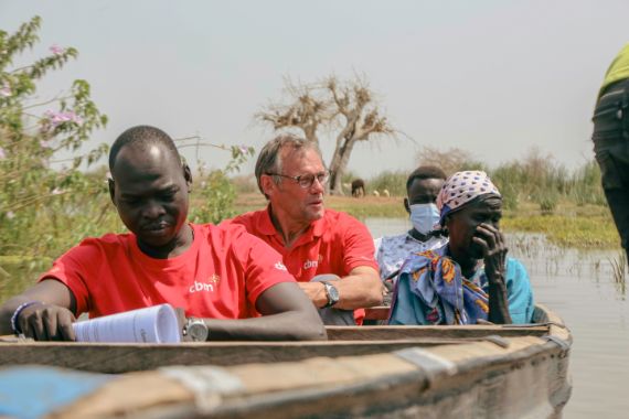 The CBM team, Samuel and Johan, escort a person affected by trachoma to surgery by boat. South Sudan is affected by conflict and climate change. 