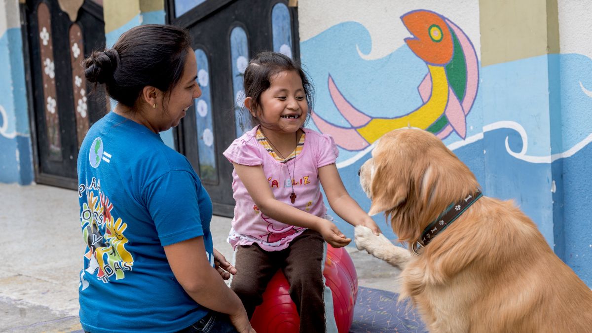 A young girl playing with a dog. A teacher is close by