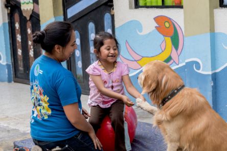 A young girl playing with a dog. A teacher is close by