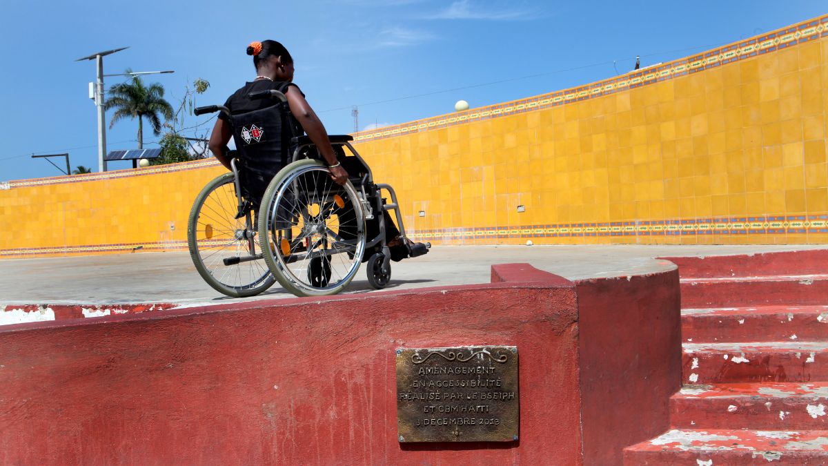 Eine Frau im Rollstuhl neben einer Treppe.