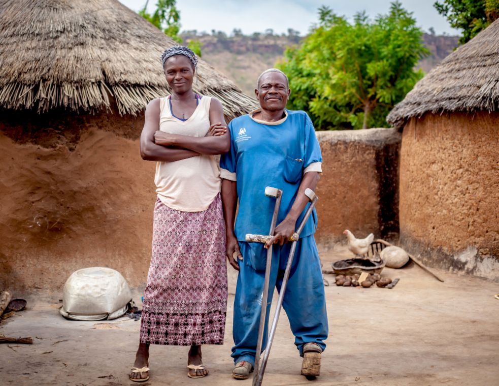 Two people standing in front of their hut. 